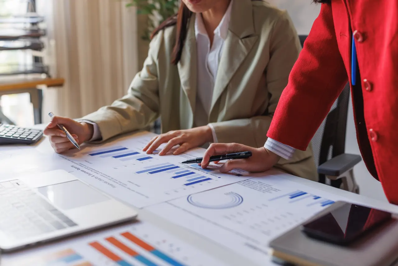 Two colleagues reviewing printed performance charts and a report together at a desk, deciding which numbers actually moved.
