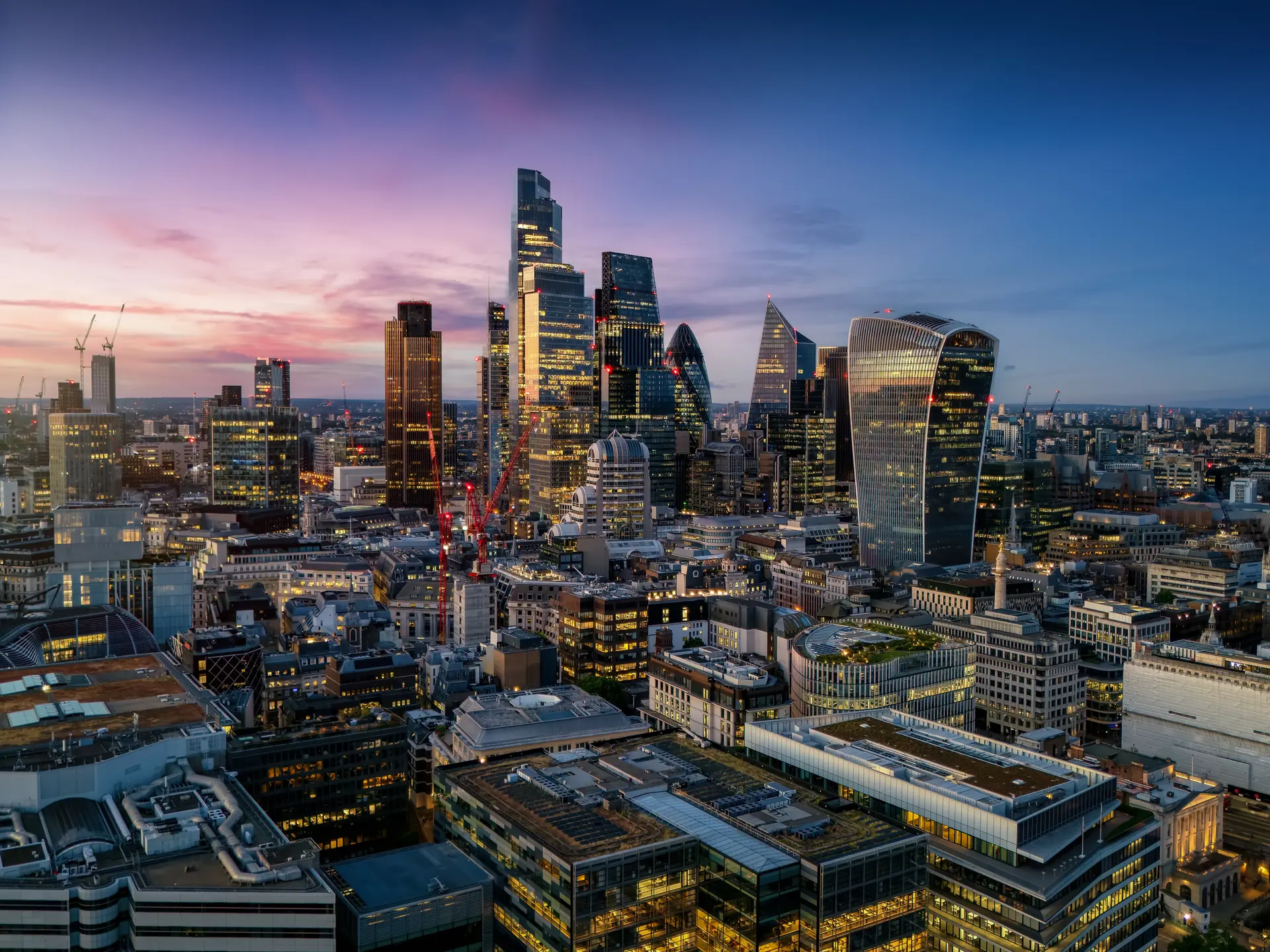 The City of London financial district lit at dusk, seen from above.